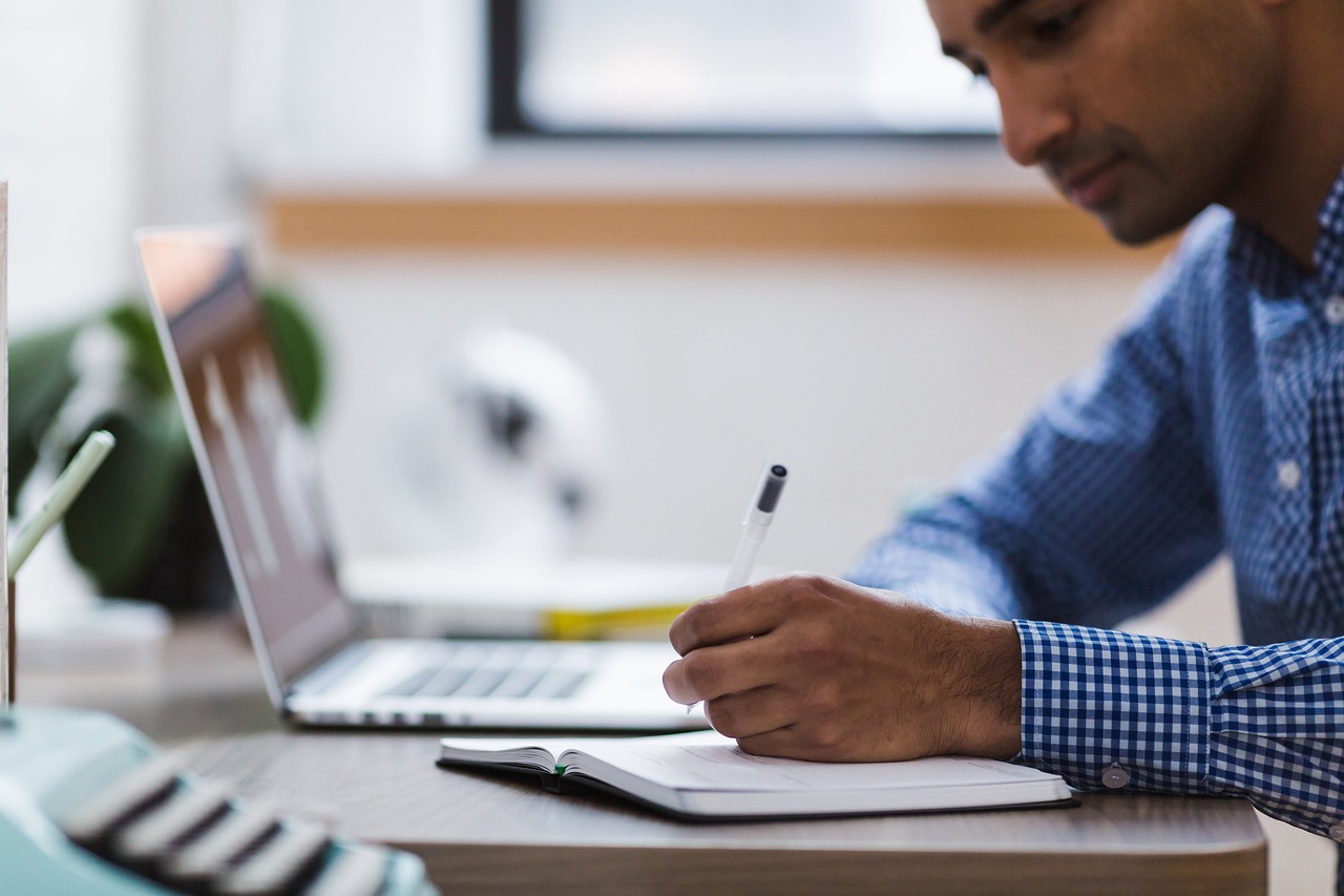 man taking notes by his computer